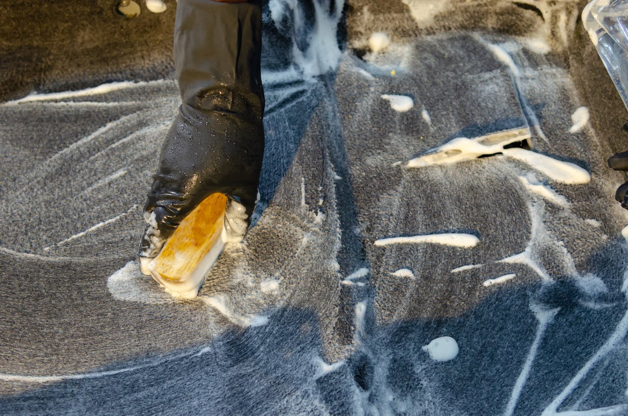 A detailed view of cleaning in progress, focusing on a gloved hand using a brush with detergent on a surface.
